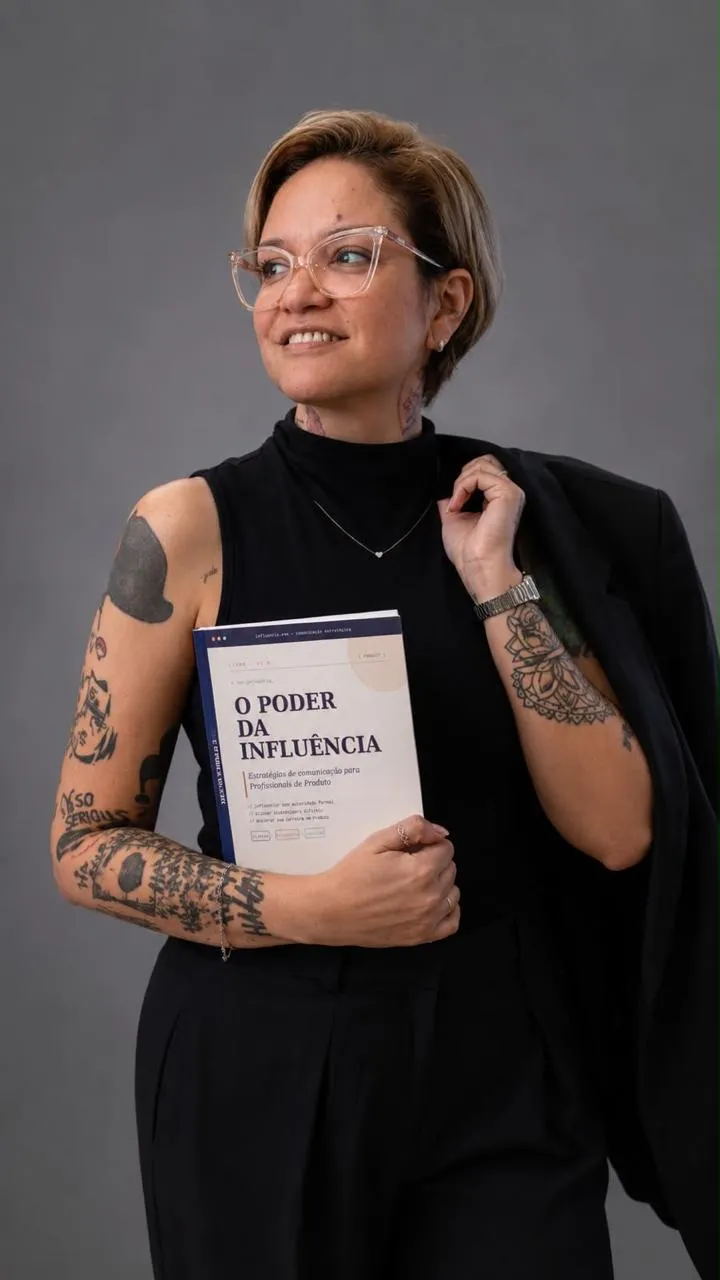 Fernanda Carvalho sorrindo, de blazer sobre o ombro, segurando o livro O Poder da Influência